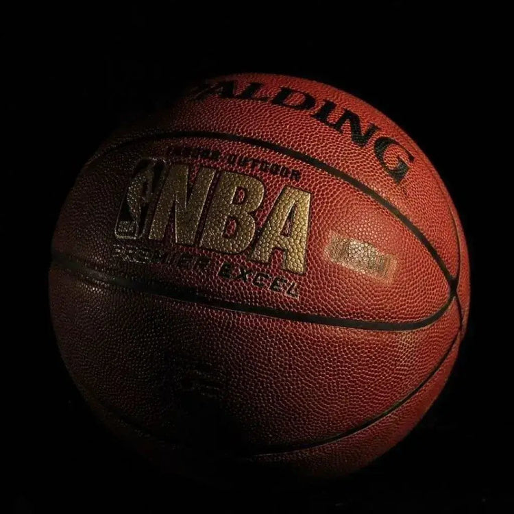 In a shadowy room, a basketball stands out, its vibrant texture contrasting with the surrounding darkness.