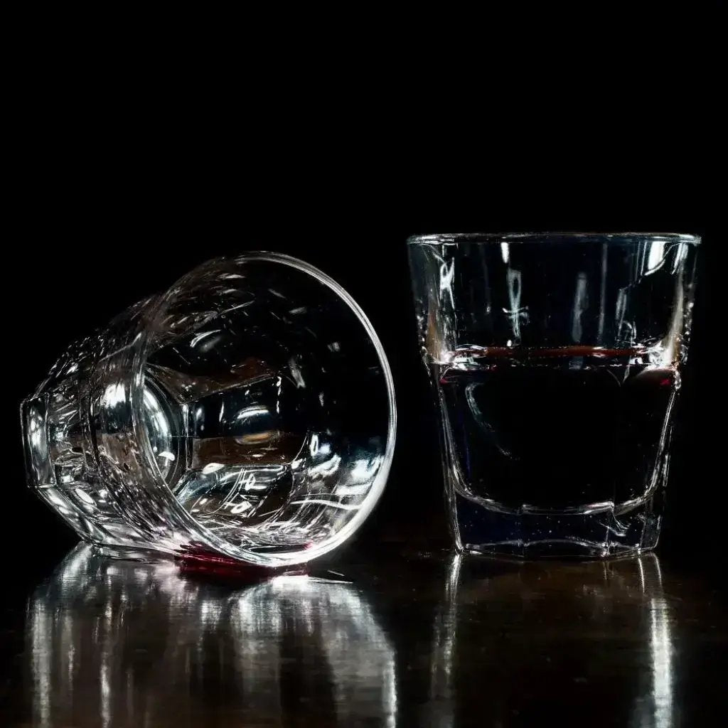 Two elegant empty glasses one filled with rich red liquid the other empty, resting gracefully on a sleek black surface.