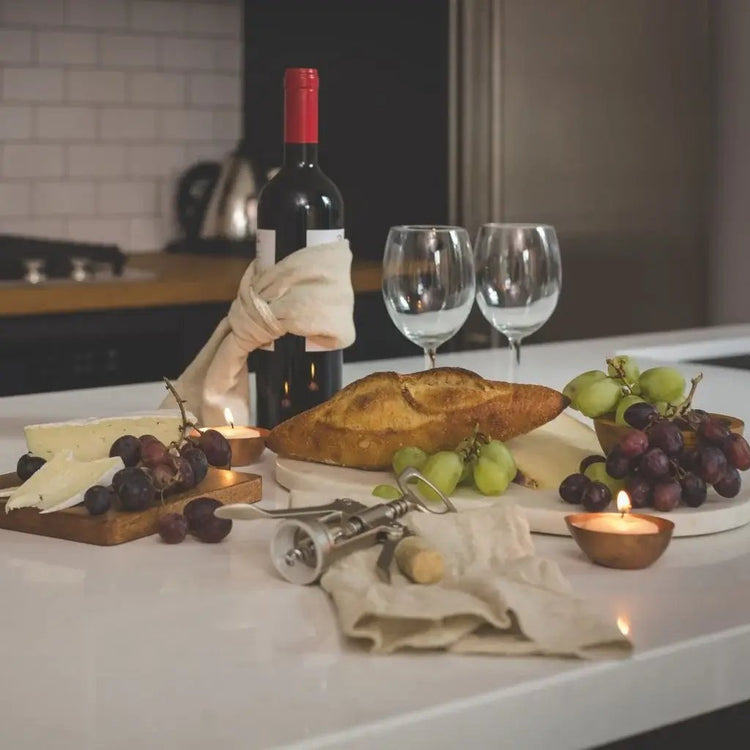 A kitchen counter displaying a bottle of wine, a loaf of bread, and a cluster of grapes, creating a cozy dining atmosphere.