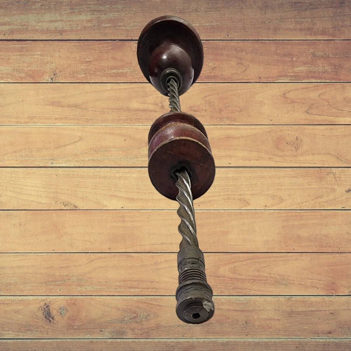 A wooden floor with an antique drill and handle made of wood lying on it.
