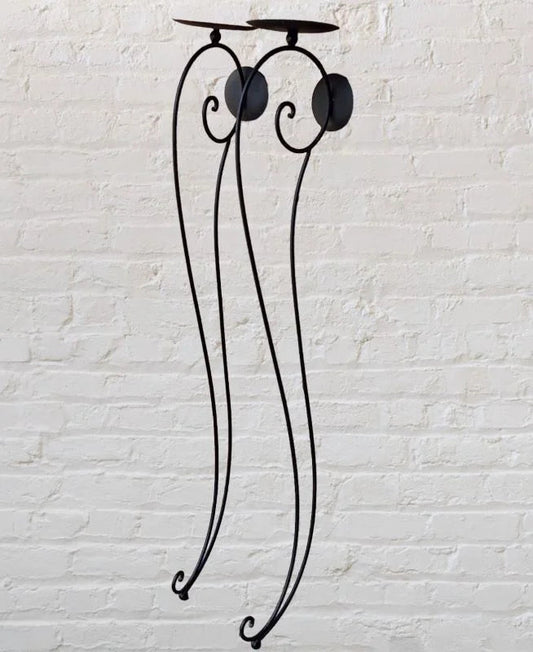 A black iron candle holder with two lit candles on top.