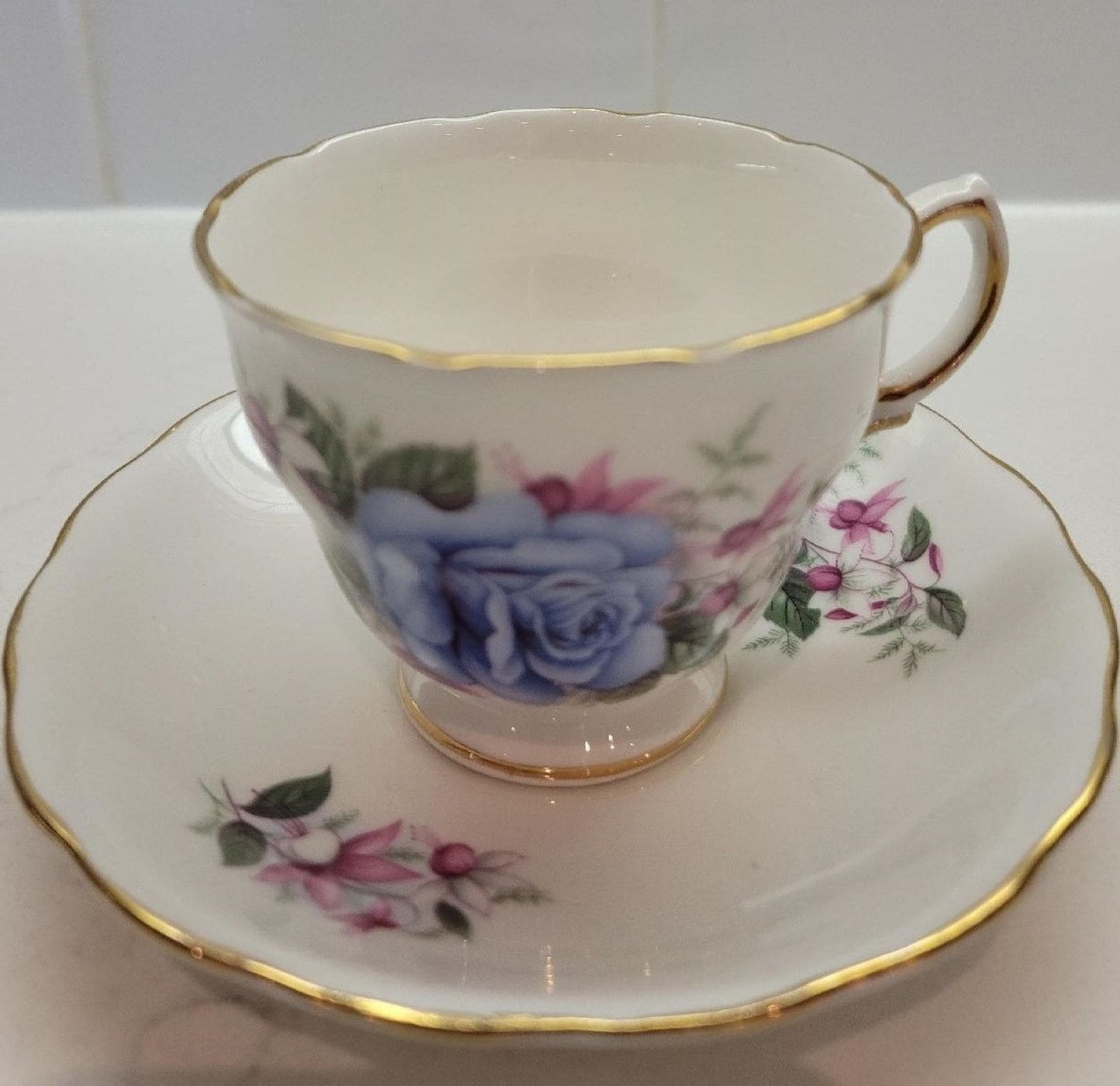 A tea cup and saucer featuring a delicate blue rose design.