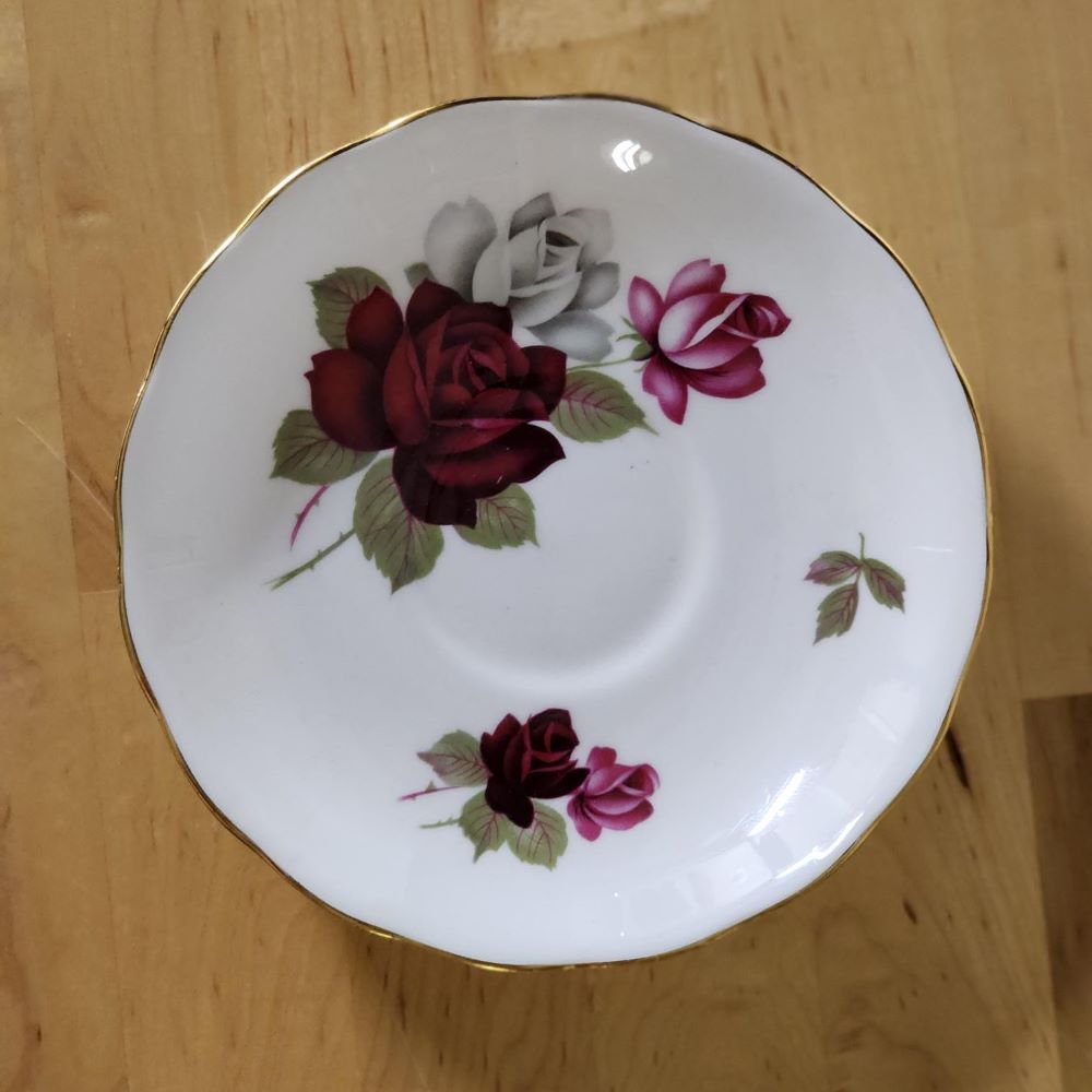 A teacup with dark red roses placed on top of books.