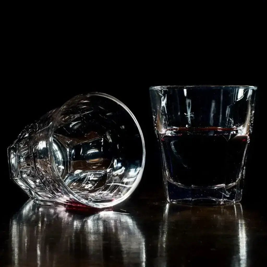Two glasses one empty one with red liquid sitting on a table.
