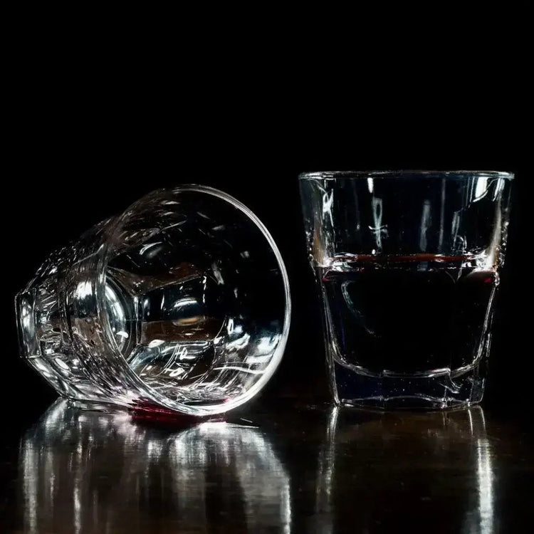 Two glasses one empty one with red liquid sitting on a table. Glassware 