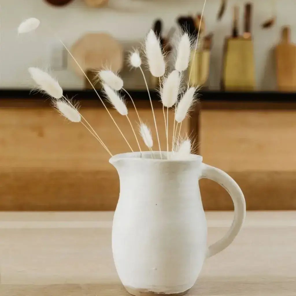 A white ceramic pitcher with tall grasses, part of our home collection for your viewing pleasure.