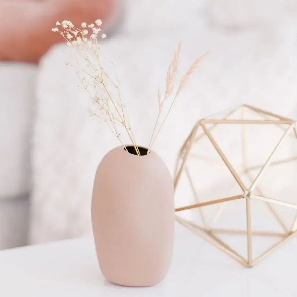 A pink vase with dried grass on a white table for kitchen and dining collection.