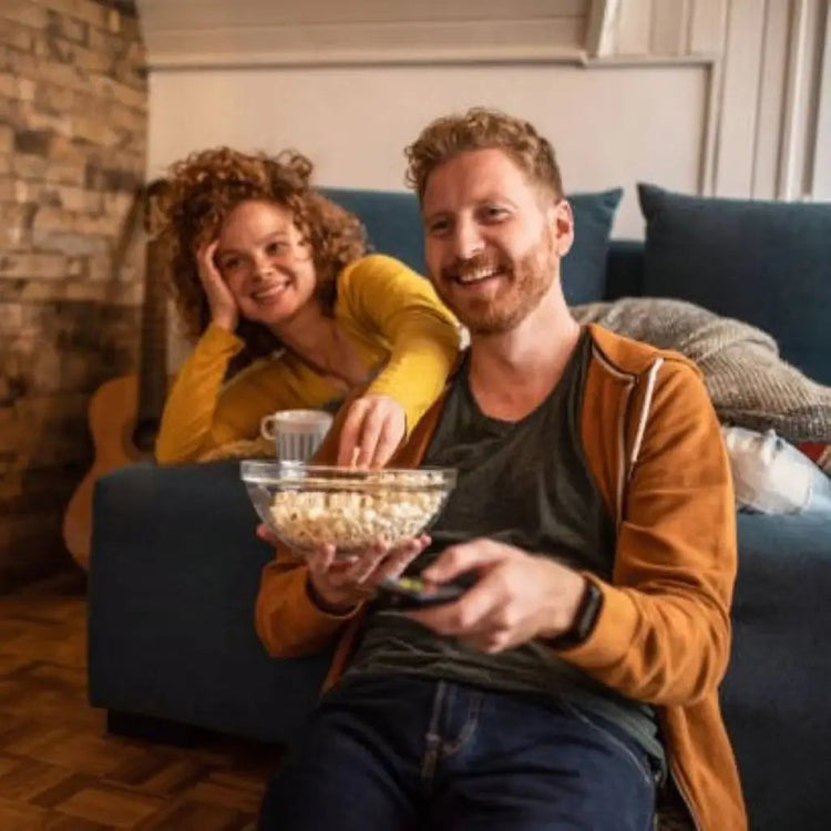 A couple enjoying a cozy evening at home, watching their favorite TV series together while munching on popcorn.