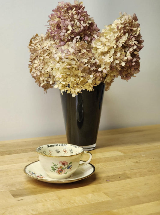 Teacup and Saucer Set on a wood desk with flowers in a vase.