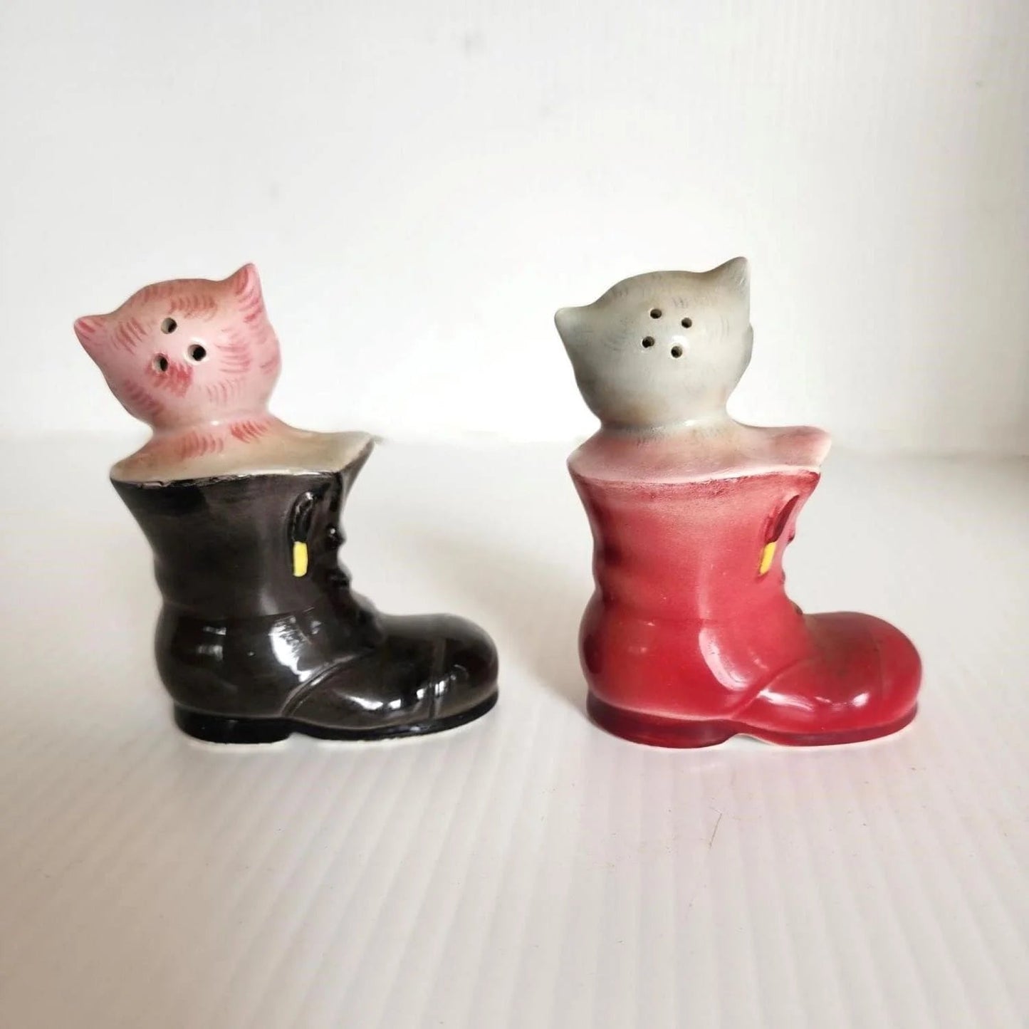 Two ceramic cat figurines sitting in boots, showcasing a charming and whimsical display of feline companionship.