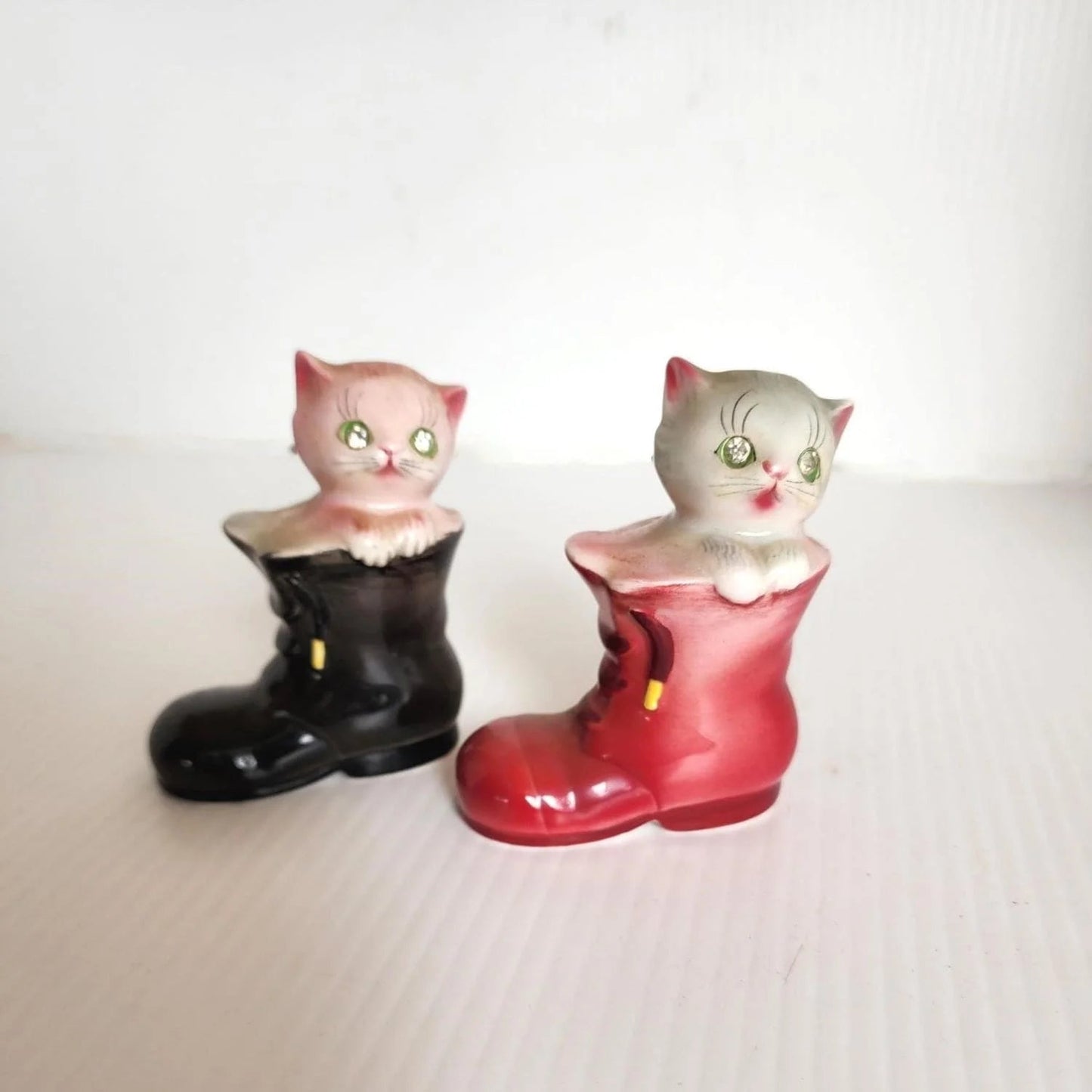 Two ceramic cat figurines sitting in boots, showcasing a charming and whimsical display of feline companionship.
