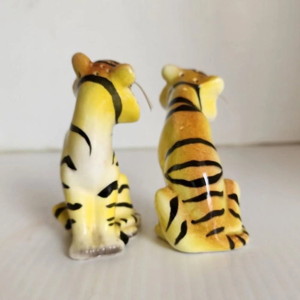 Two ceramic tiger salt and pepper shakers sitting on a table, showcasing intricate details and a lifelike appearance.