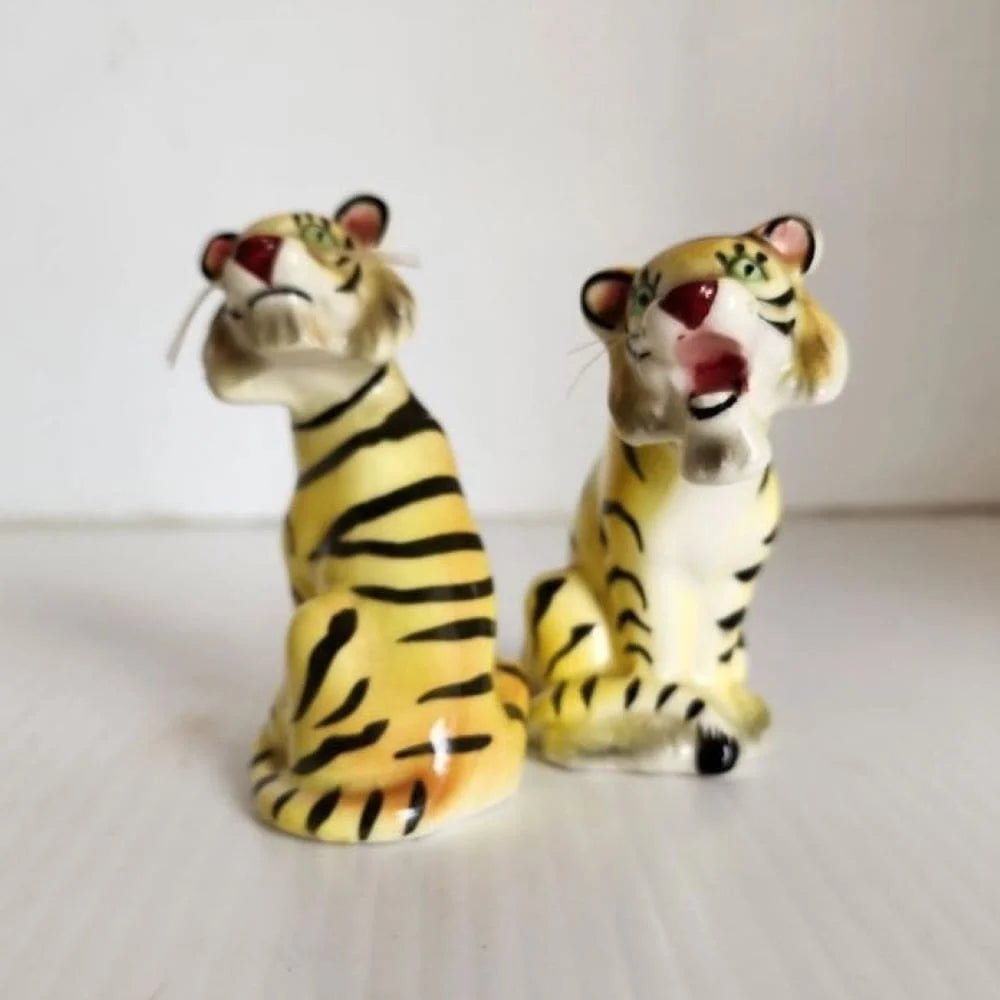 Two ceramic tiger salt and pepper shakers sitting on a table, showcasing intricate details and a lifelike appearance.