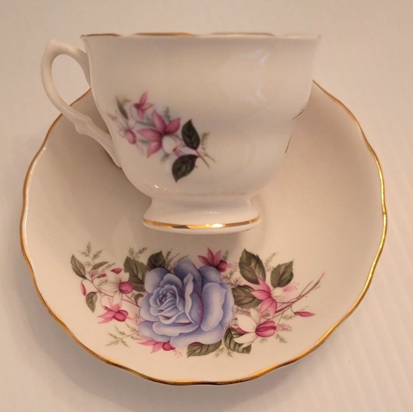 A tea cup and saucer featuring a delicate blue rose design.