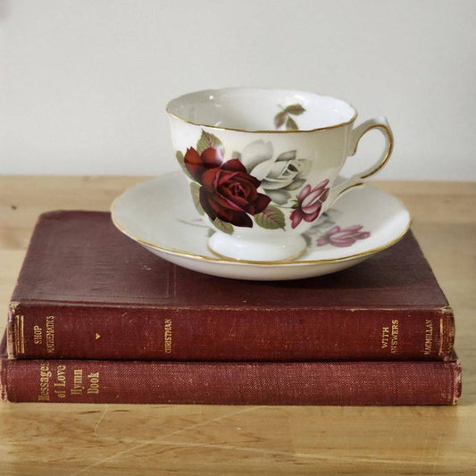 A teacup with dark red roses placed on top of books.
