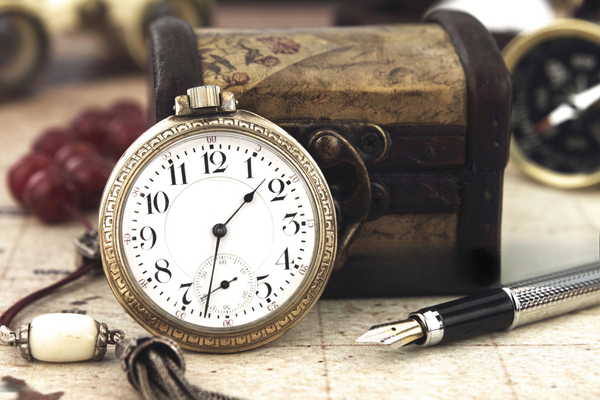 Pocket watch leaning against a box with a pen in the foreground