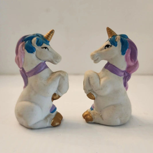 Two ceramic unicorn figurines sitting on a table, one white and one pink, with intricate details and a glossy finish.
