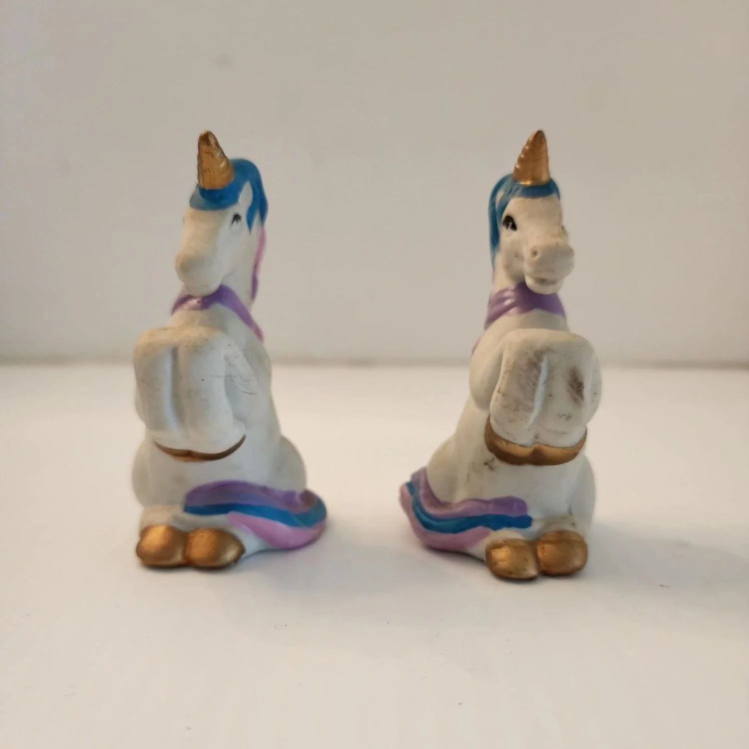 Two ceramic unicorn figurines sitting on a table, one white and one pink, with intricate details and a glossy finish.