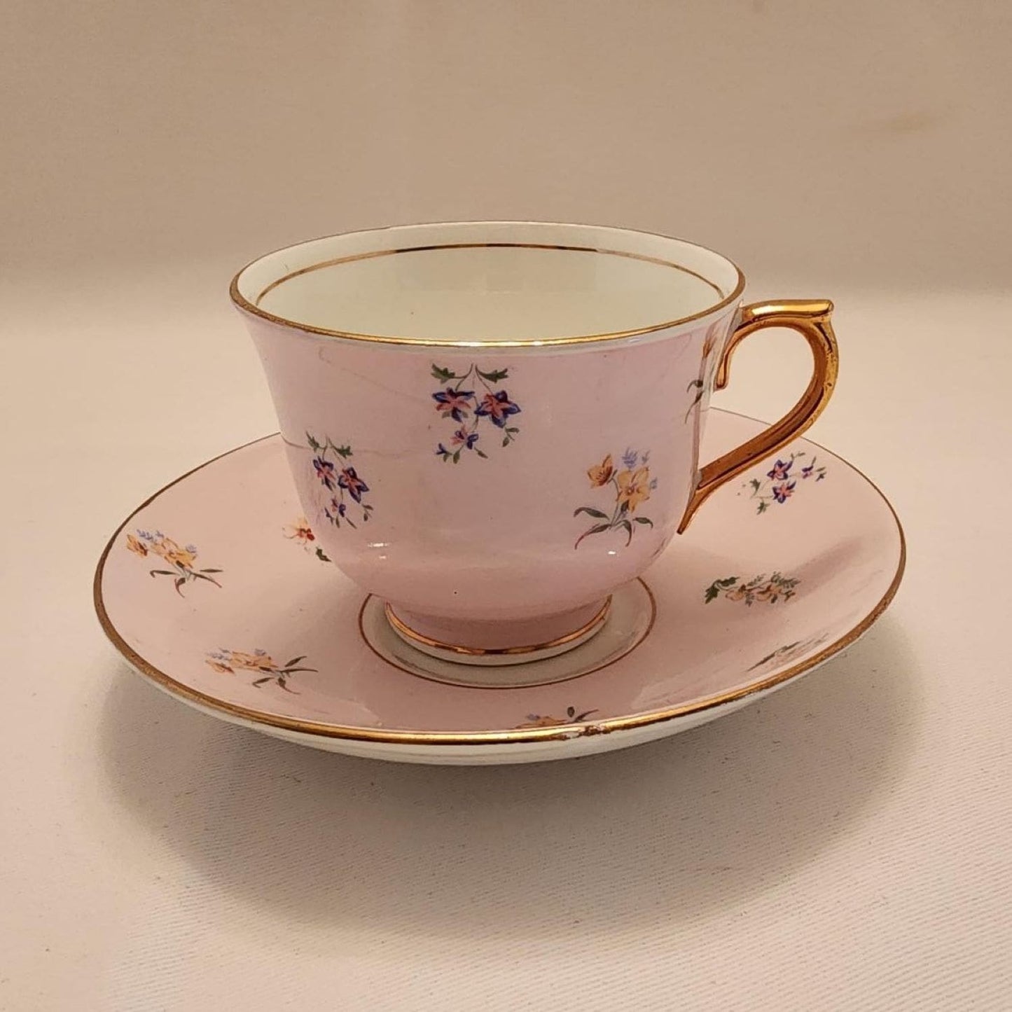 A pinkish teacup and saucer with delicate floral patterns.